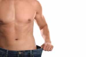 Man holding loose jeans after a male mini tummy tuck to achieve a sculpted lower abdomen and remove stubborn fat.
