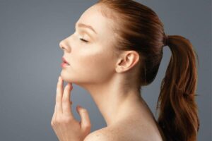 Young woman’s side profile with hand near chin, symbolizing rhinoplasty vs septoplasty surgical choices.