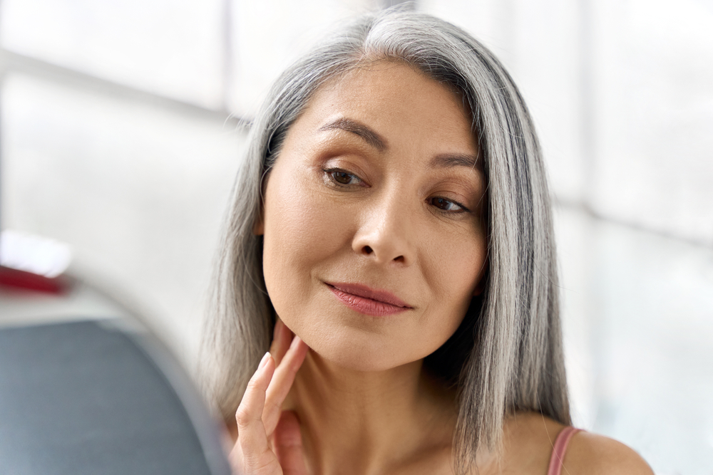 Mature woman examining her face in mirror, showing smooth skin results from Botox treatment aftercare.